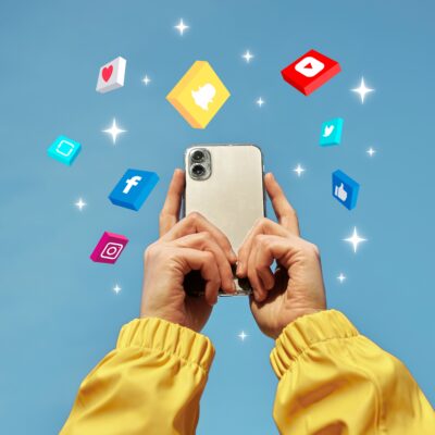 Hands play with a phone surrounded in a cloud of social media icons.